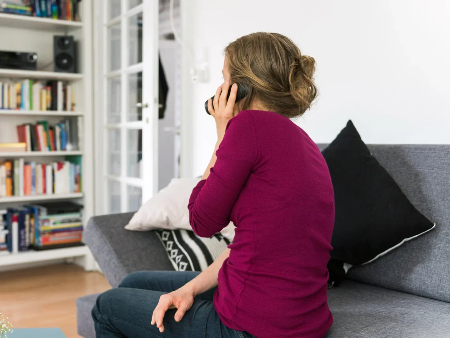 A woman sitting on a sofa talking on the phone, seen from behind.